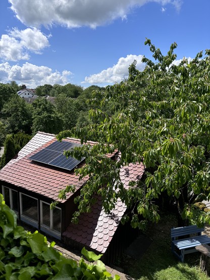 Ein Dach mit montierten Solarpanels. Davor eine hellblaue Holzbank. Der Himmel ist nur noch leicht bewölkt.